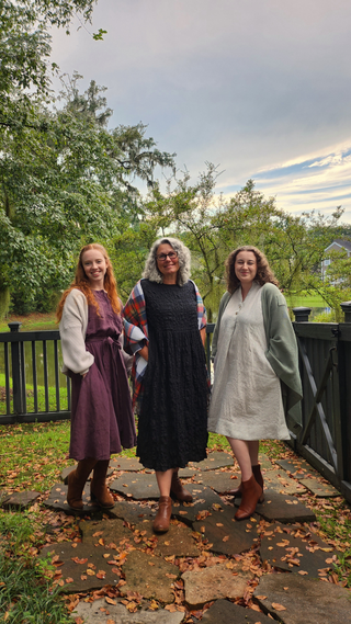 three women wearing fall dresses made of linen. Accessorized with scarves and boots. Fall dress style. Purple linen dress. Black Dress. striped white linen dress.